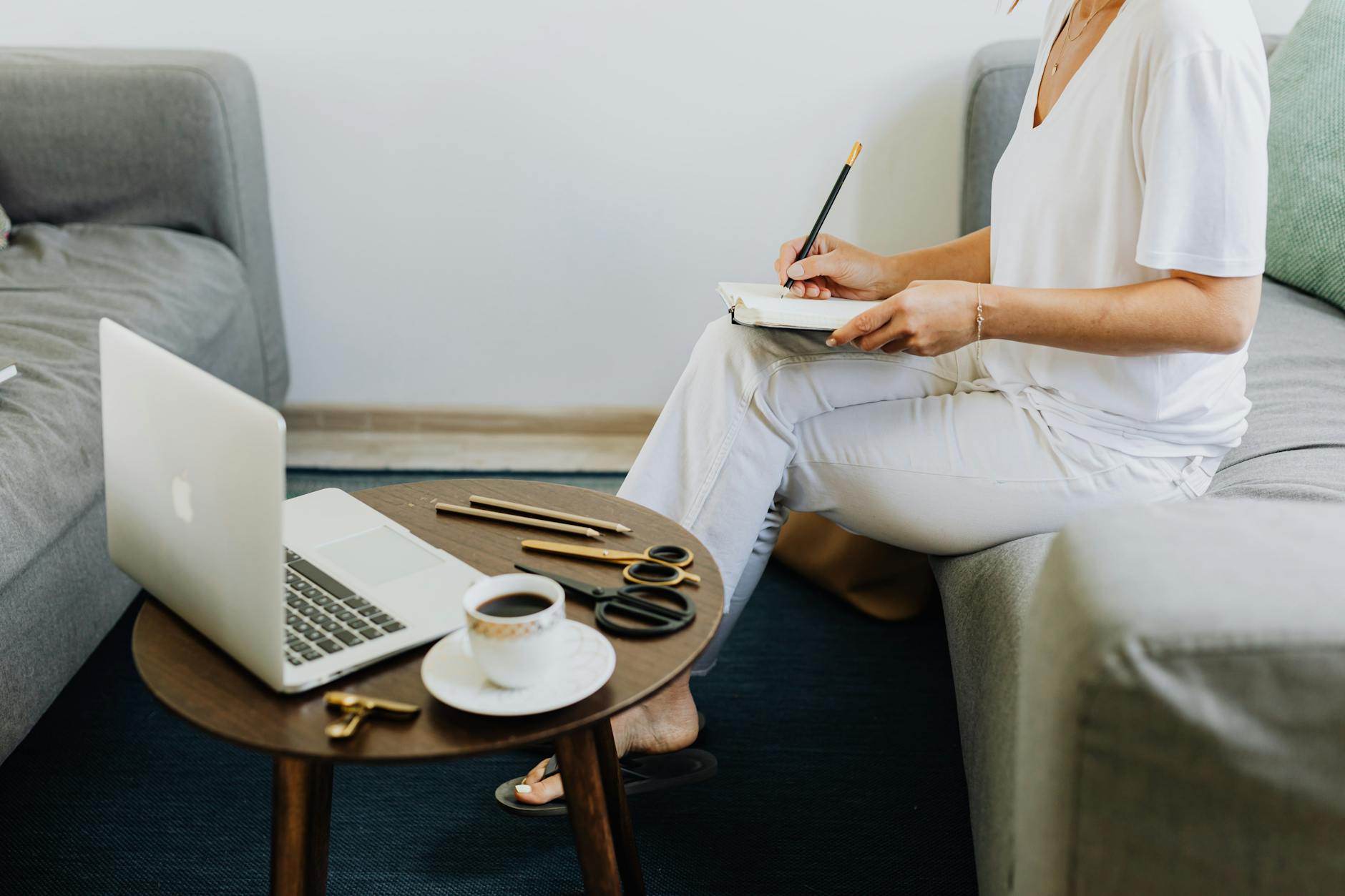 woman in white shirt sitting on couch while writing on notebook