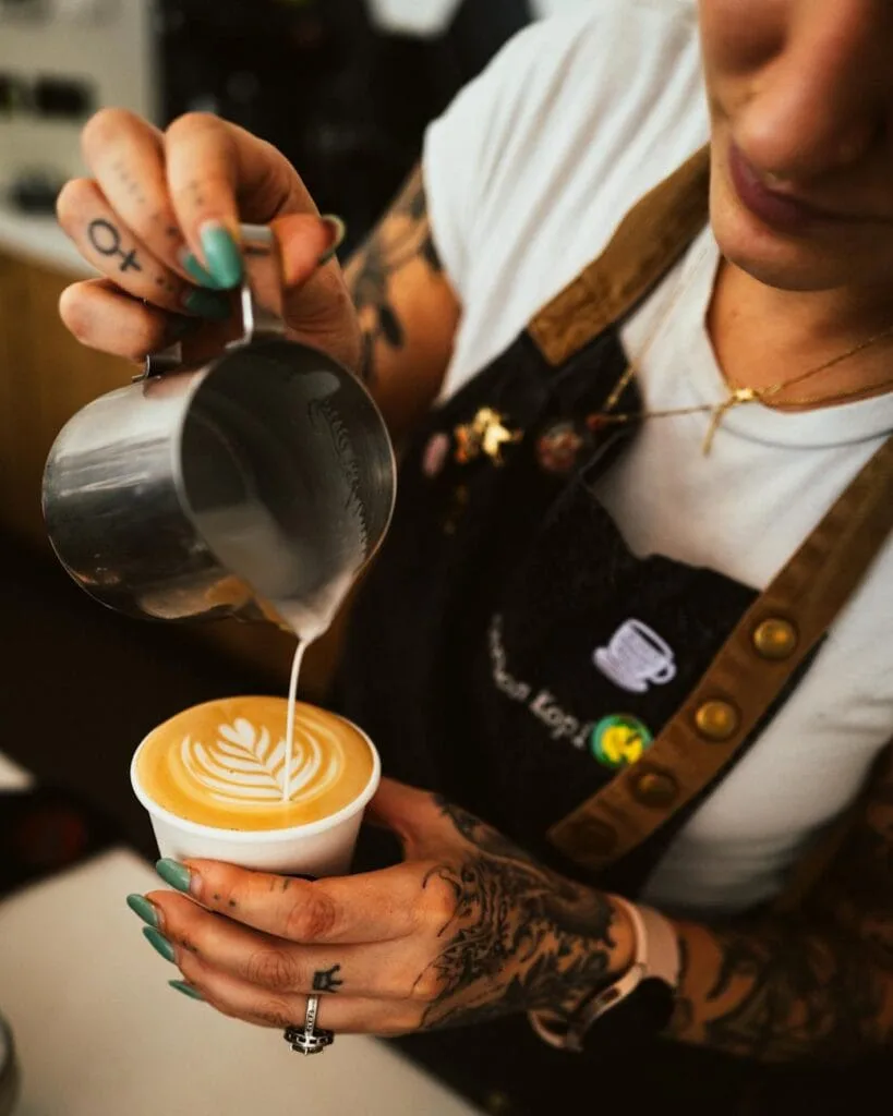woman pouring milk to coffee at cafe
