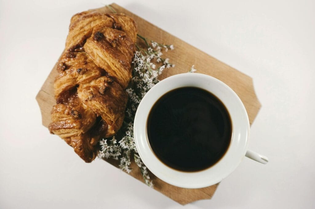 white ceramic teacup filled with coffee near baked bread