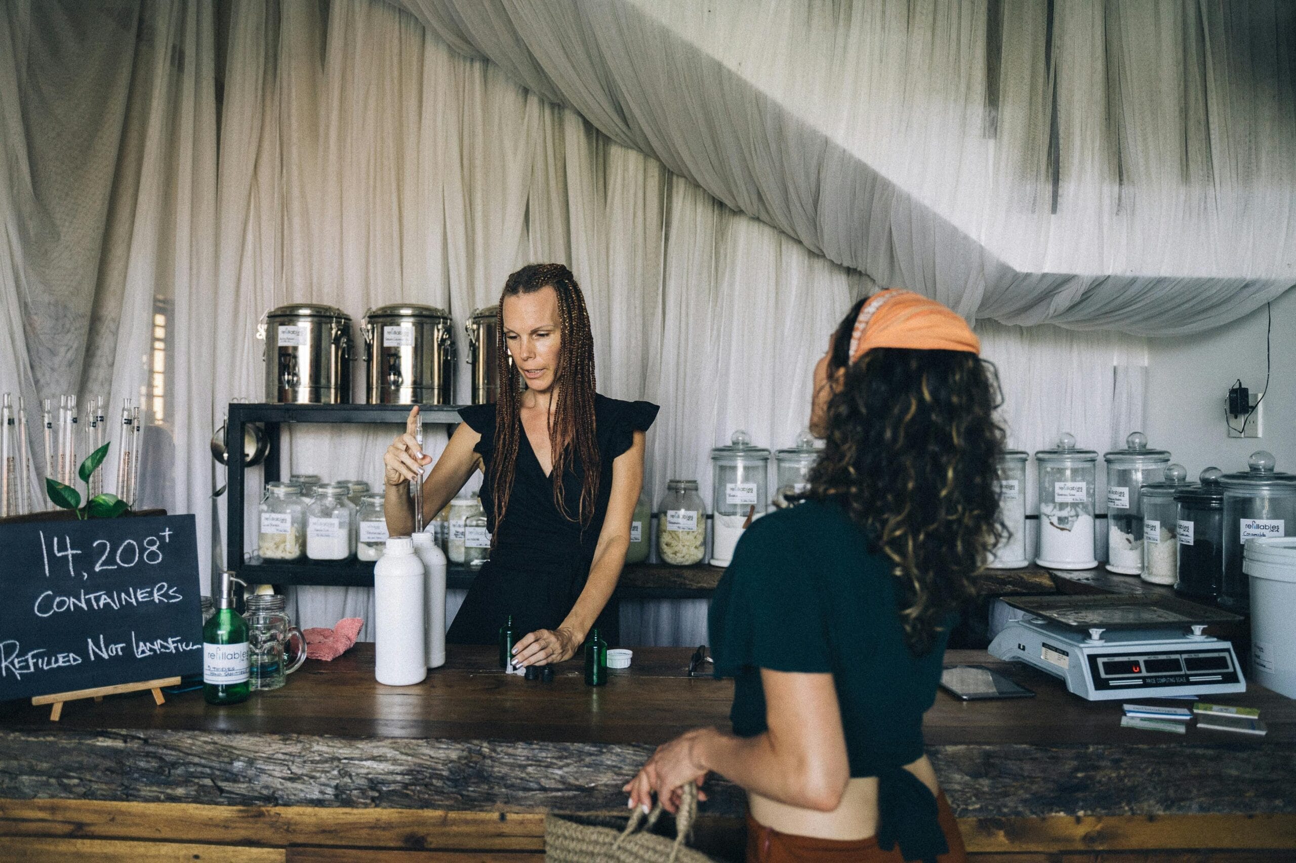 Two women engage at a sustainable refill station with reusable containers.
