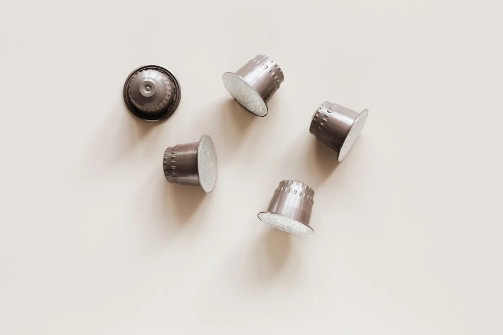 Minimalist photograph of several silver coffee capsules on a light background, perfect for coffee-related projects.