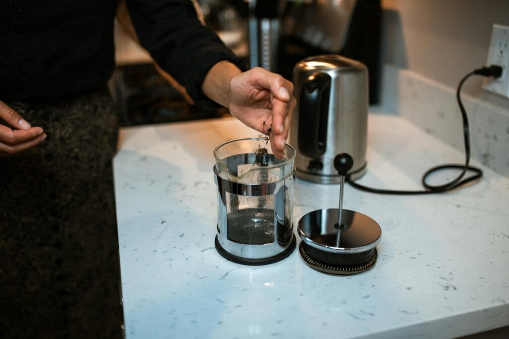 Person making coffee using a French press on a kitchen counter.