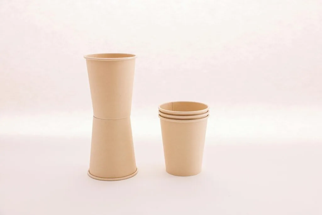 A minimalist setup featuring a stack and a single paper cup against a soft white background.