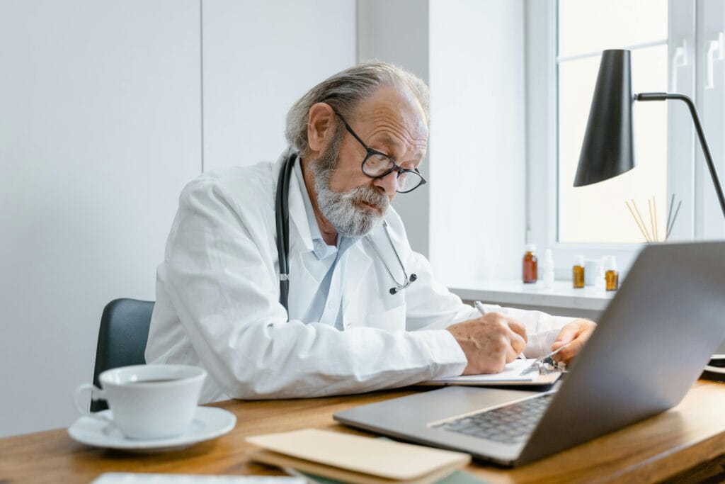 Experienced senior doctor writes a prescription online in a bright, modern office. specialty coffee