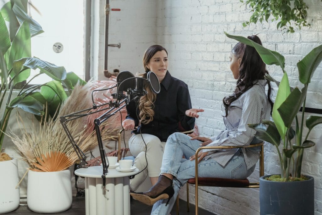 Two women engaged in a lively conversation during a podcast recording session in a modern studio.